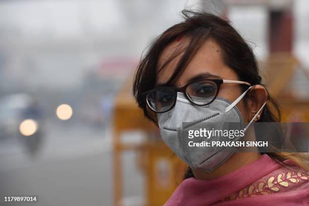 Woman wearing a protective face mask waits for public bus in smoggy conditions in New Delhi on November 4, 2019. - Millions of people in India's...