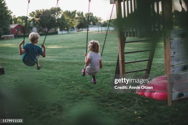 back view of children swinging - family garden play area photos et images de collection