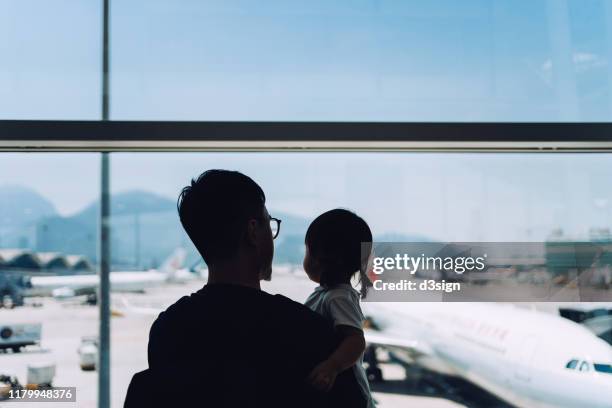 silhouette of joyful young asian father embracing cute little daughter looking at airplane through window at the airport while waiting for departure - kid looking through window stock pictures, royalty-free photos & images