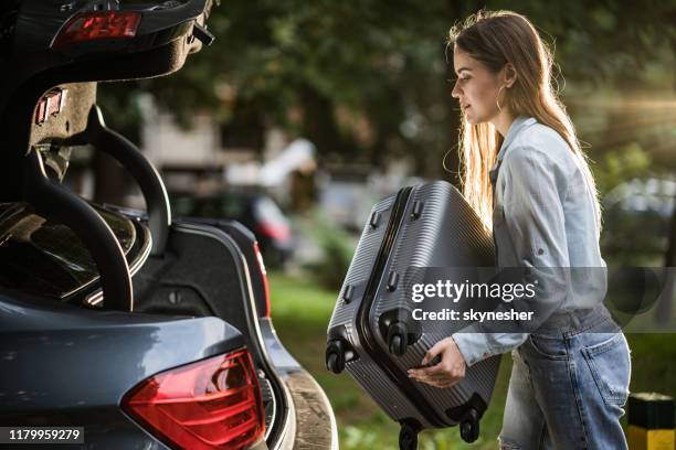 mulher nova que carrega sua bagagem no tronco de carro. - car trunk - fotografias e filmes do acervo