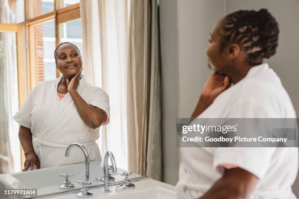 afro-amerikaanse vrouw kijkt naar haar teint in een badkamer - smiling mature eyes stockfoto's en -beelden