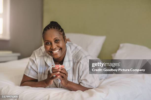 glimlachend afro-amerikaanse vrouw liggend op haar bed koffie drinken - africa cup of nations 2010 abuja stockfoto's en -beelden