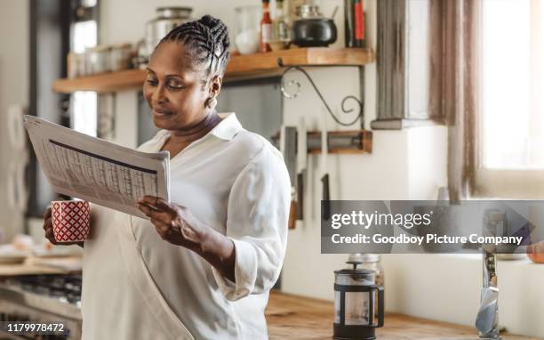 lächelnde afroamerikanische frau liest die zeitung am morgen - zeitung im broadsheet format stock-fotos und bilder