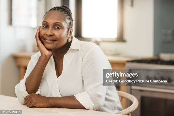 sonriendo mujer afroamericana sentada en su cocina en casa - parte de una serie fotografías e imágenes de stock