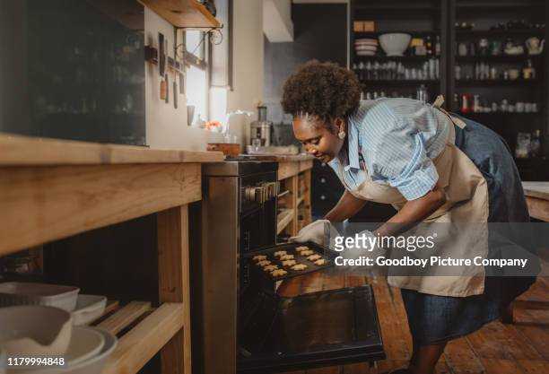 mature african american woman taking cookies out of her oven - baking tray stock pictures, royalty-free photos & images