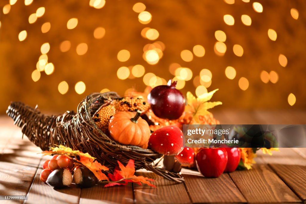Thanksgiving still life with cornucopia pumpkins and illuminated background on a rustic wooden table