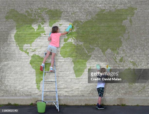 a young girl and a young boy cleaning dirt off a world map mural. - global solutions stock-fotos und bilder