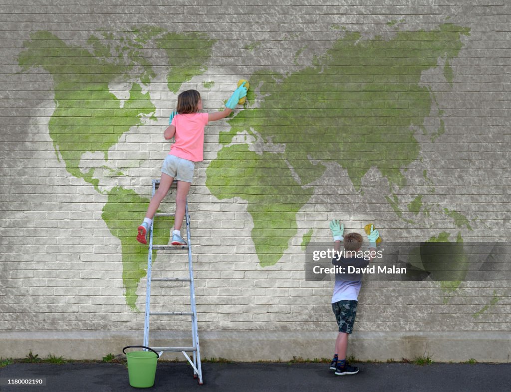 A young girl and a young boy cleaning dirt off a world map mural.