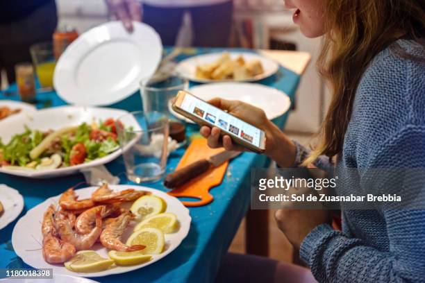 girl looking at the smartphone at the table while having dinner with the family - kin in de hand stock-fotos und bilder