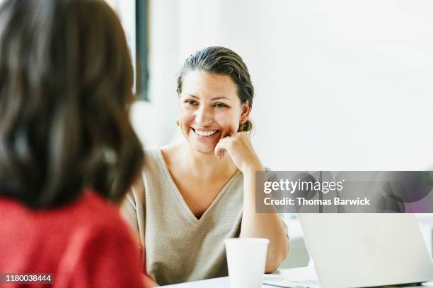 smiling businesswoman in discussion with colleague during meeting in office conference room - colleagues in discussion in office conference room fotografías e imágenes de stock