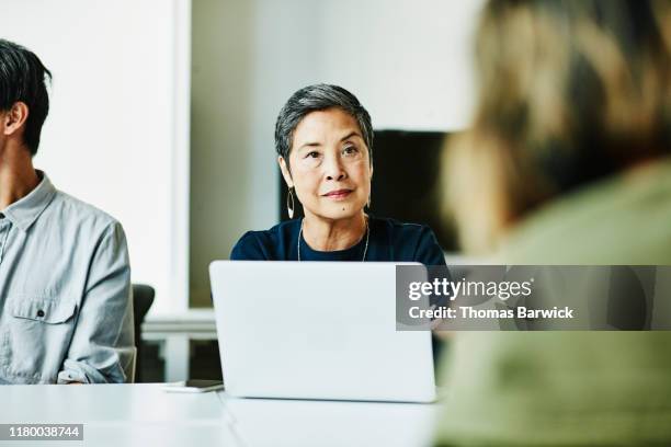 senior businesswoman listening to presentation during meeting in office conference room - filipino woman fotografías e imágenes de stock