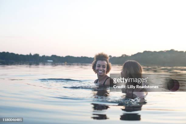 two young women laughing while swimming in a lake together - adult swim stock-fotos und bilder
