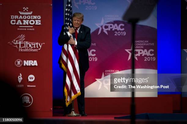 President Donald Trump hugs a U.S. Flag as he takes the stage at CPAC in National Harbor, Maryland Saturday March 2, 2019.