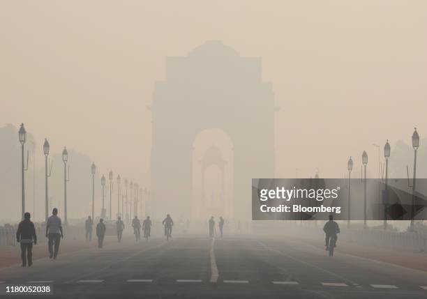 Pedestrians walk along Rajpath boulevard as India Gate monument stands shrouded in smog in New Delhi, India, on Tuesday, Nov. 5, 2019. Air pollution...