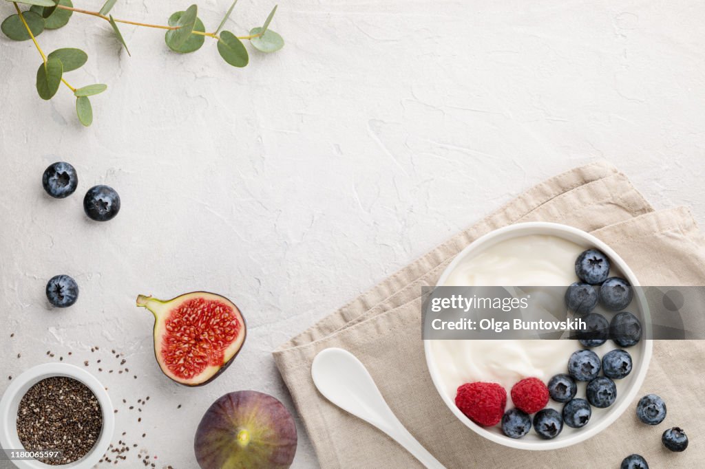 白色發酵優酪乳與藍莓，無花果，嘉種子和覆盆子在淺灰色的桌子上碗
