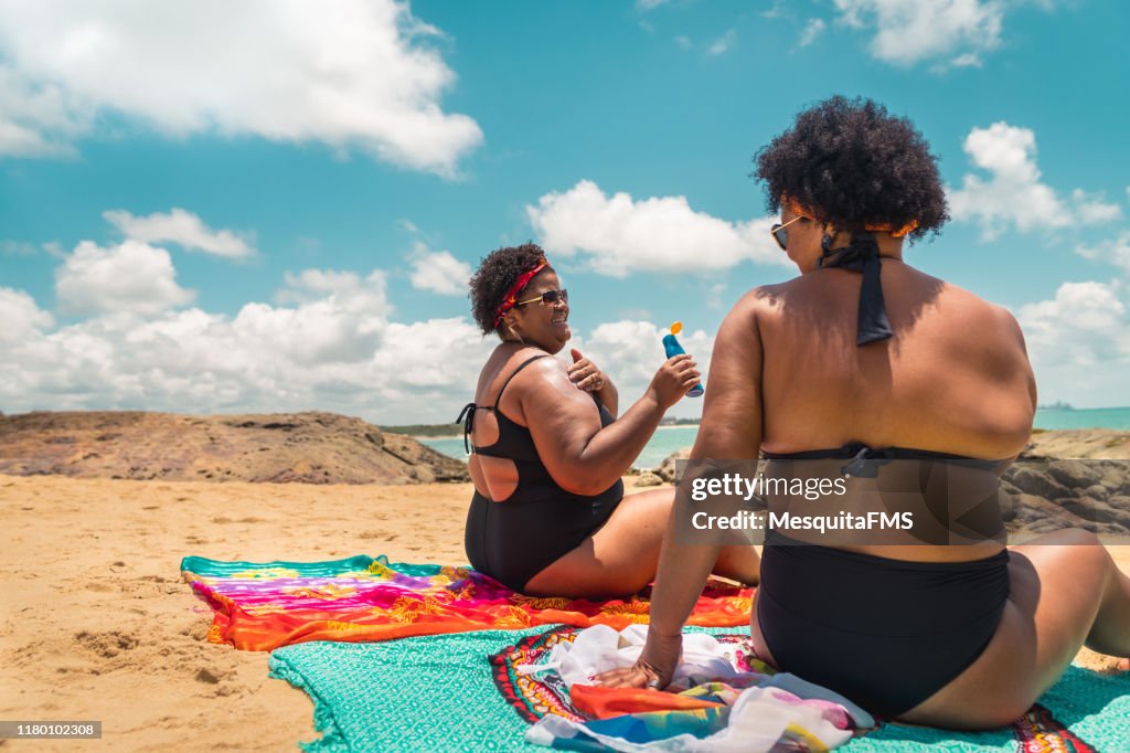 Rear view of afro women using suntan lotion at beach