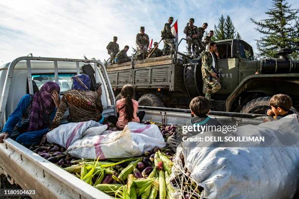 Syrian government soldiers ride in the back of a truck with national flags past a pickup truck carrying women and children seated above harvested...