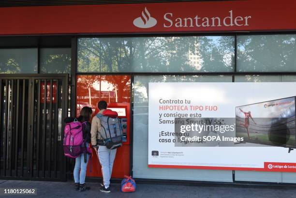 Customers withdraw cash from an automated teller machine operated by Santander bank in Madrid. Banco Santander will close another 411 bank branches...