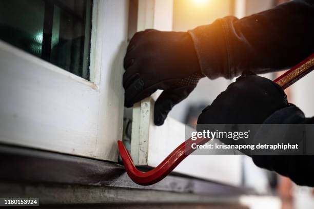 dangerous masked burglar with crowbar breaking into a victim's home door,concept - crime or recreational drug or prison or legal trial stock-fotos und bilder