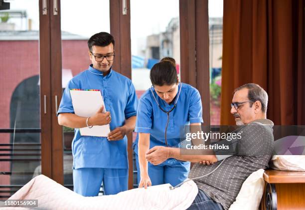 male and female nurse checking senior man's blood pressure on house call - home carer stock pictures, royalty-free photos & images