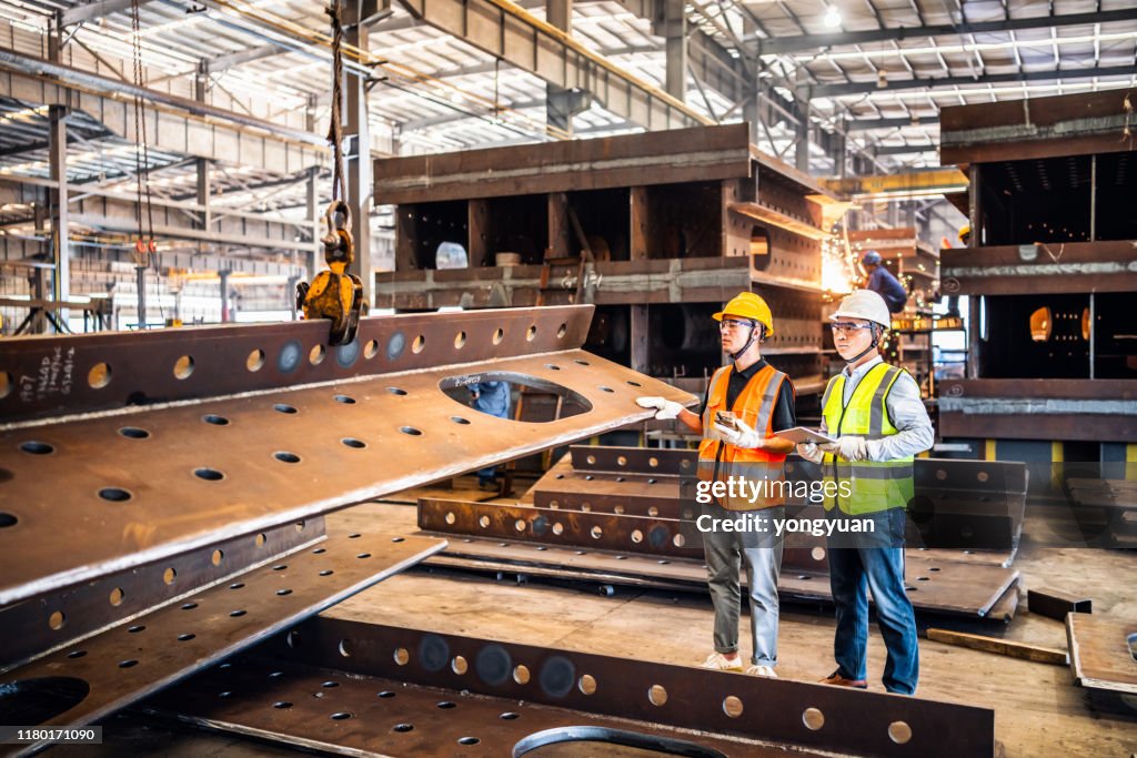 Two metal workers operating a crane in a steel factory