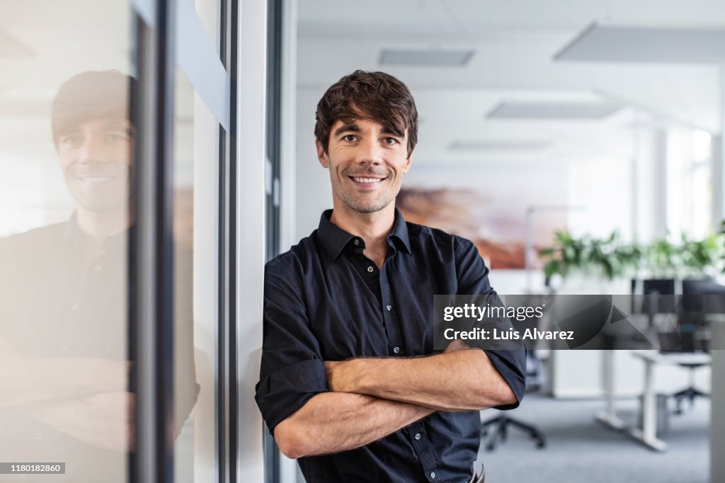 Confident businessman leaning on wall in creative office