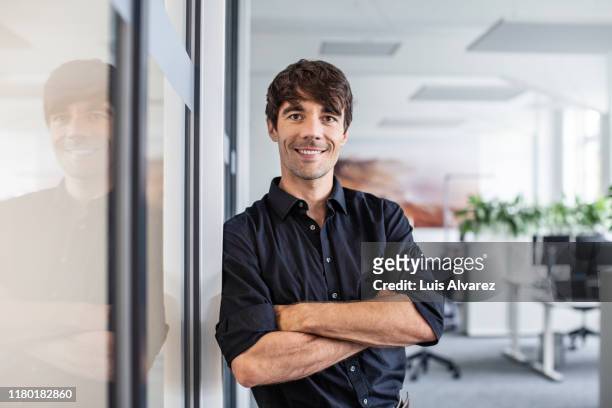 confident businessman leaning on wall in creative office - mid adult stock-fotos und bilder