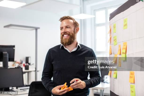 confident businessman standing by bulletin board in office - hipster office stock pictures, royalty-free photos & images
