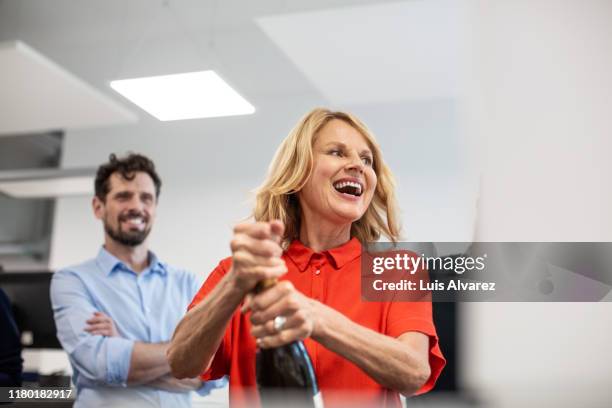 businesswoman opening champagne bottle in office - beförderung arbeit stock-fotos und bilder