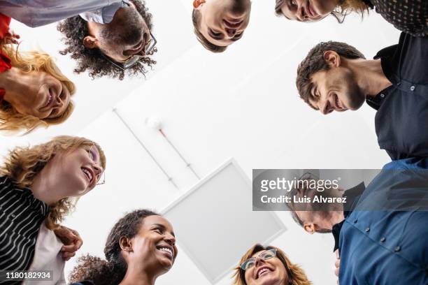 smiling entrepreneurs huddling together in creative office - zusammenhalt stock-fotos und bilder