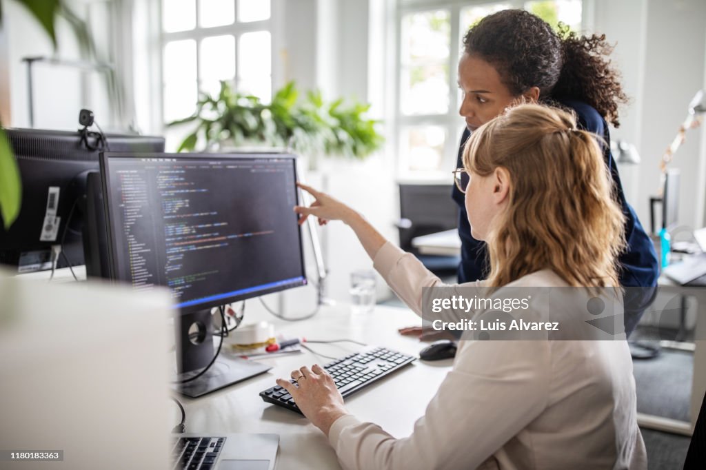 Coworkers discussing computer program in office