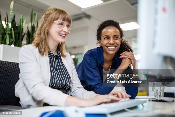 female colleagues smiling while looking at computer - collega d'ufficio foto e immagini stock