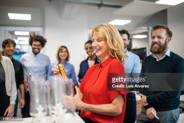 businesswoman opening champagne bottle in office - beförderung arbeit stock-fotos und bilder