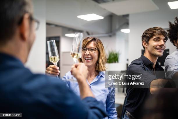 businesswoman toasting champagne flute with colleague in office - work party - fotografias e filmes do acervo