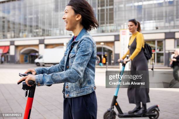 cheerful woman riding push scooter in city - city break stock pictures, royalty-free photos & images