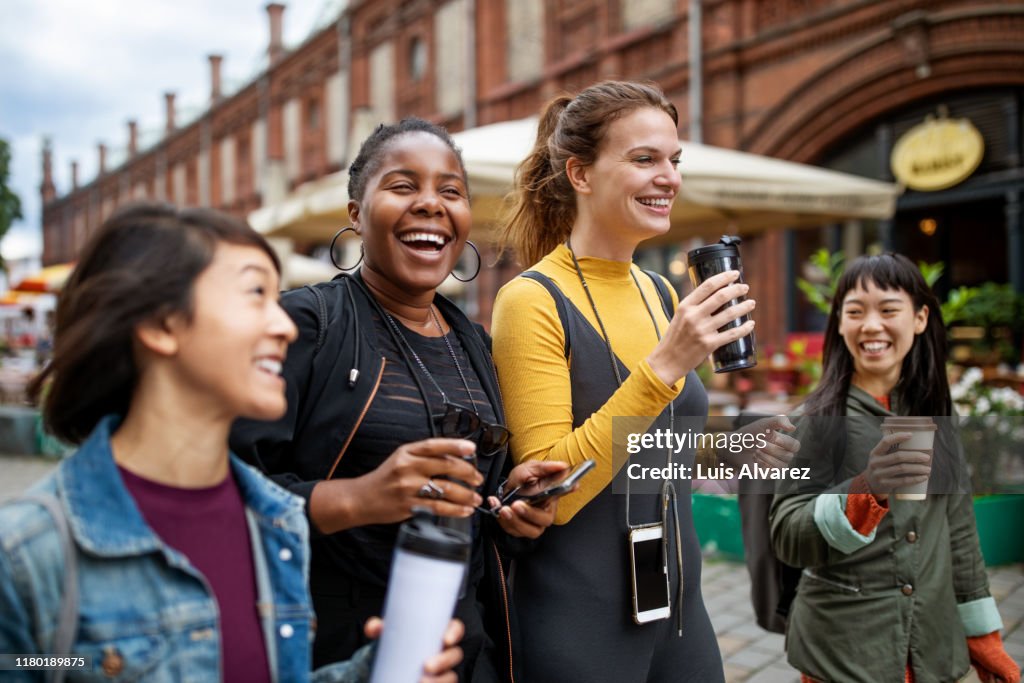 Happy female friends with drinks walking in city