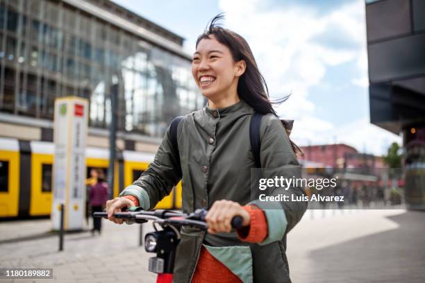 cheerful woman riding push scooter in city - motorized vehicle riding stock-fotos und bilder