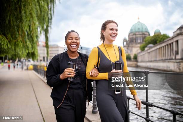 cheerful friends walking on footpath by river in city - erwachsener über 30 stock-fotos und bilder