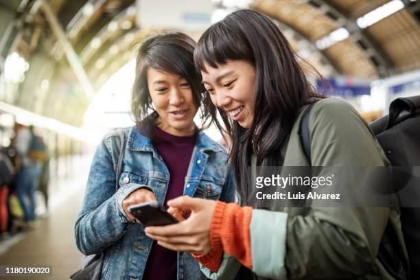 female friends using mobile phone at railroad station - two people travelling stock pictures, royalty-free photos & images