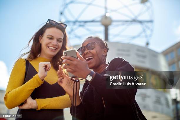 woman showing mobile phone to friend in city - escapade urbaine photos et images de collection