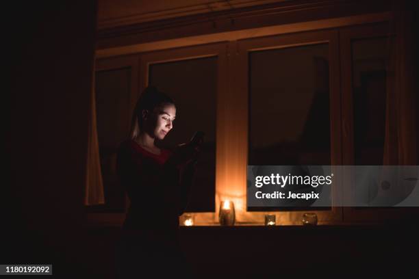 bella donna che usa il telefono nella stanza buia - candela attrezzatura per illuminazione foto e immagini stock