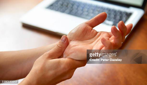 woman massaging painful wrist at work repetitive strain injury - giuntura foto e immagini stock