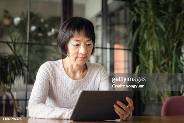 senior chinese woman using a digital tablet - asian cinema stock pictures, royalty-free photos & images