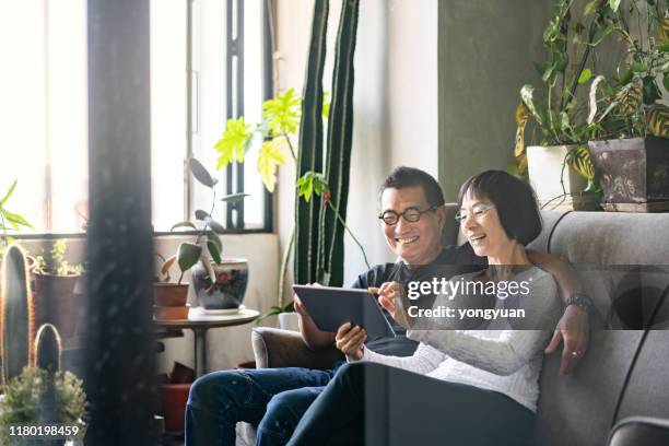 asian couple using a digital tablet on sofa - senior comfortable stock pictures, royalty-free photos & images