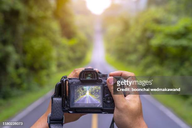 the hand of a photographer holding a camera on an empty road - digital camera stock pictures, royalty-free photos & images