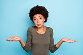 I dont care. Portrait of doubtful negative curly hair afro american girl cant choose answer solve trouble shrug shoulders hold hands hesitate wear beautiful outfit isolated blue color background