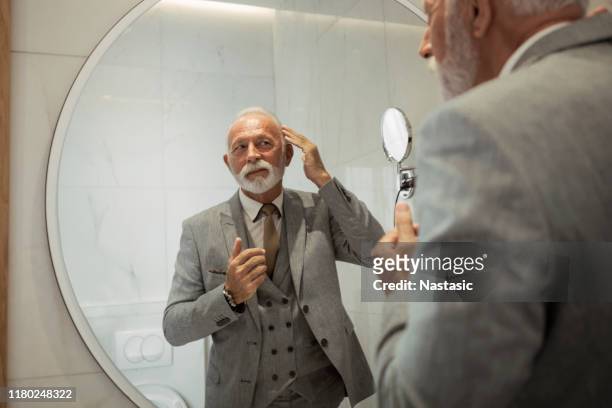 senior zakenman dressing up in badkamer - adjusting necktie stockfoto's en -beelden