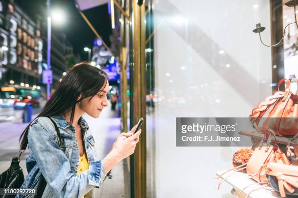 woman taking a picture to shop window at night - fashion shoot stock-fotos und bilder