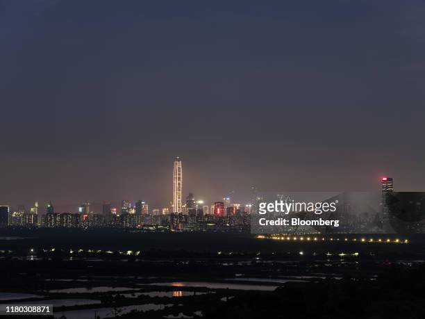 The illuminated Ping An International Finance Center , center left, and other buildings in Shenzhen stand on the horizon beyond farmland at dusk in...