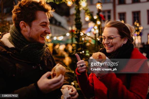 young man and woman eating hot dogs on christmas market - heidelberg germany stock pictures, royalty-free photos & images